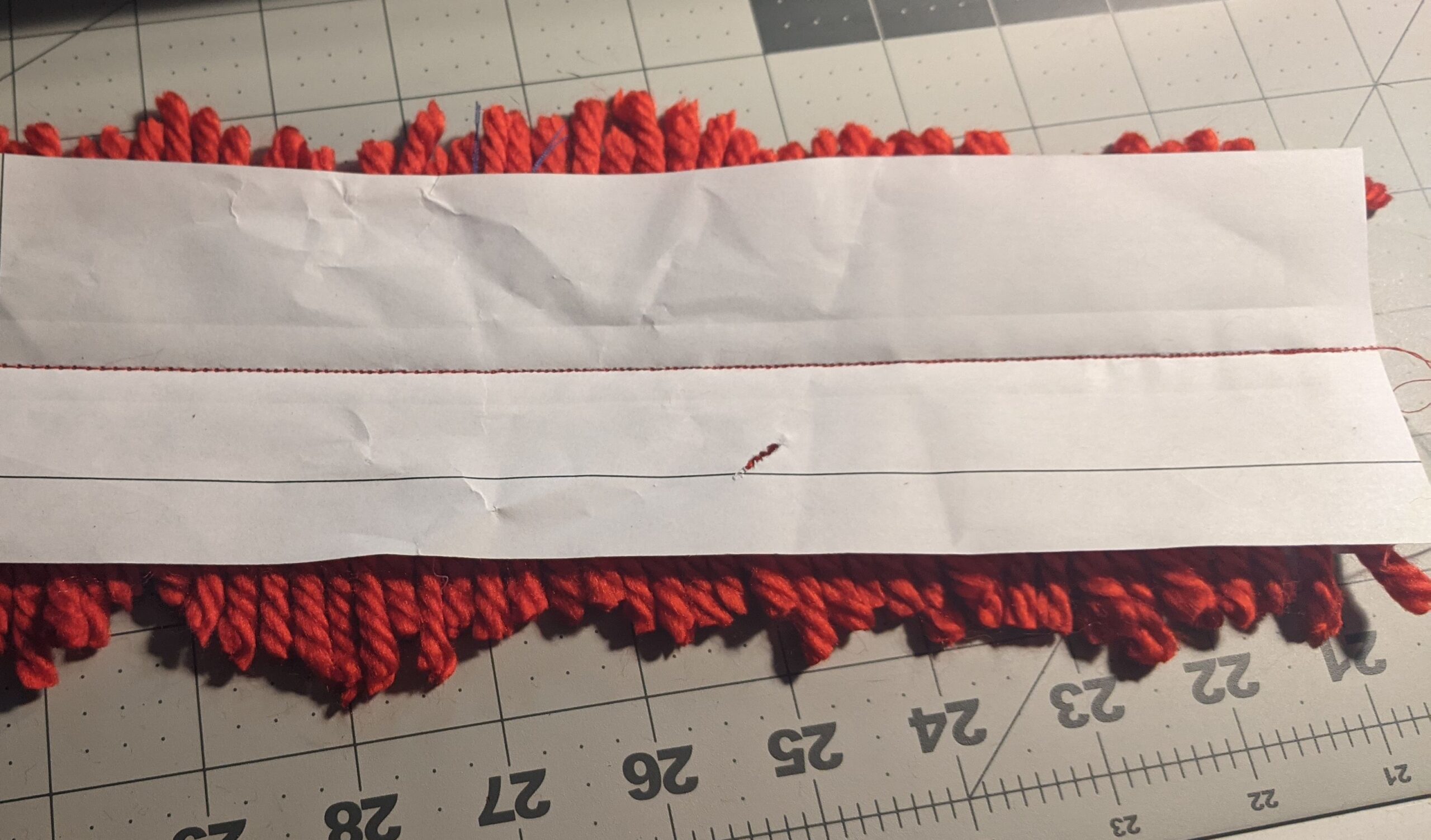 Red yard sewn side by-side to paper, showing stitching. On a cutting board.